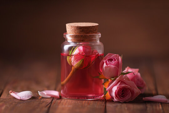 Bottle of essential rose oil and flowers on wooden table