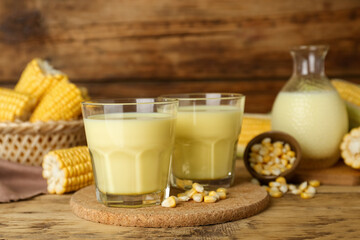 Tasty fresh corn milk in glasses and cobs on wooden table