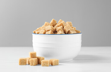 Bowl with brown sugar cubes on white table