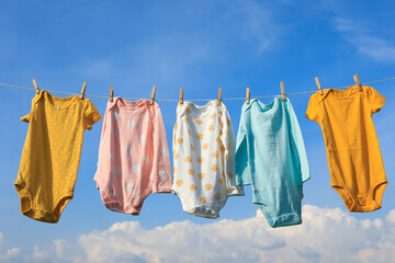 Clean baby onesies hanging on washing line against sky. Drying clothes