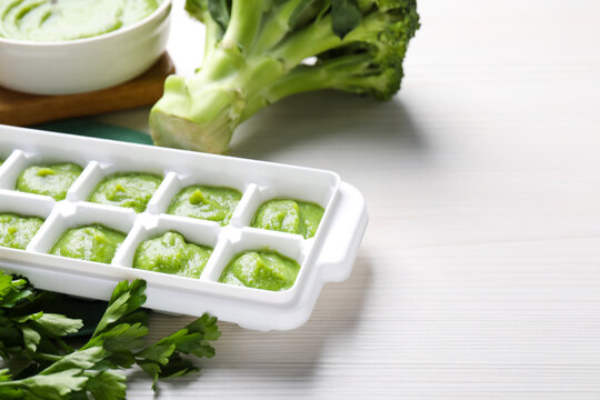 Broccoli puree in ice cube tray and ingredients on white wooden table, space for text. Ready for freezing