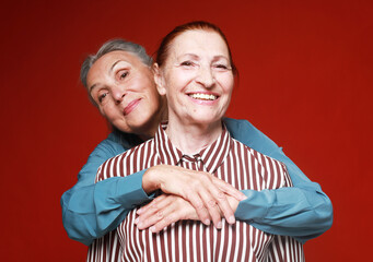 Two elderly women friends hugging on red background. Lifestyle and old people concept.