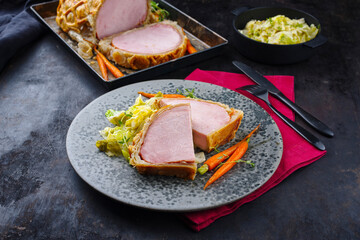 Gebackenes Kasseler Schweinesteak im Teigmantel mit Wirsing Kohl und Baby Karotten serviert als Draufsicht auf einem Nordic Design Teller und Tablett