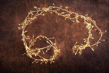 Christmas lights on a brown wood background. Golden Christmas garland top view, copyspace