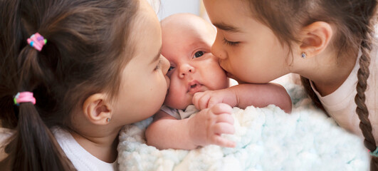 Two lovely sisters kiss their little brother. Newborn baby boy with girls. Love and friendship concept. Happy siblings. 