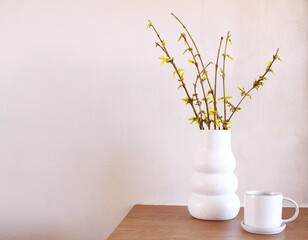 Modern white ceramic vase with yellow blooming Forsythia flowers on a vintage bench table. Scandinavian interior.
