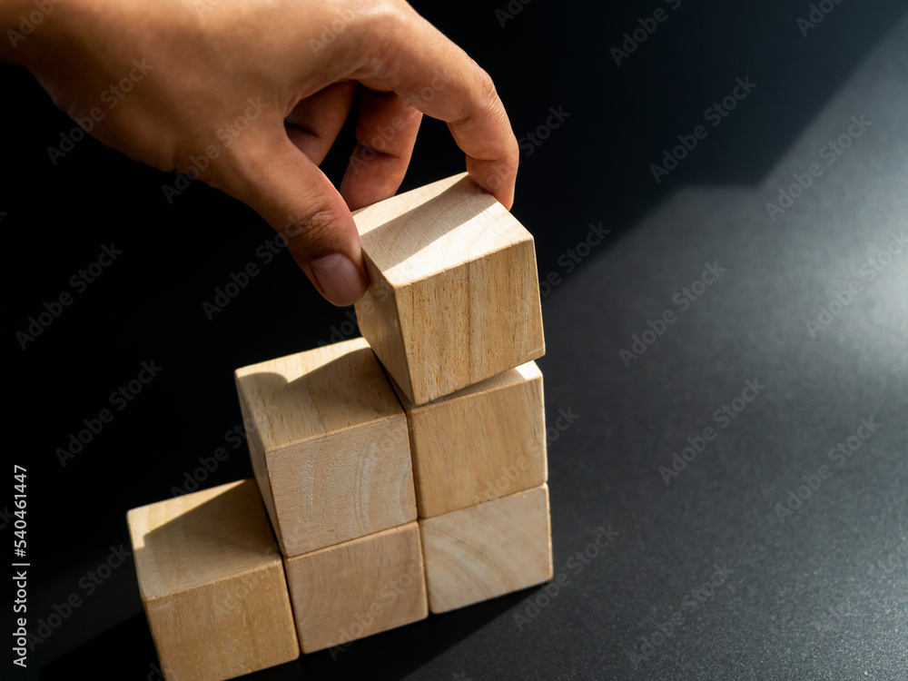 Poster closeup wooden cube block put by hand on the top of chart step on black background with copy space, 