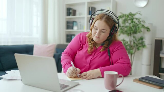 Call center woman in headset with microphone talking to client, making notes