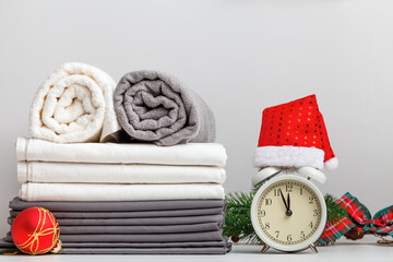 Stack of folded rolls of towels and bed sheets, sheet on table with christmas decor and alarm clock