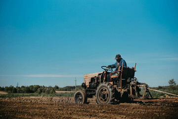 an elderly man tractor driver plows the land with plows on an old tractor.
