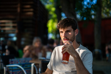 Caucasian brunette young man drinking a smoothie with a straw in a terrace