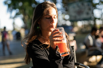 Caucasian brunette young girl drinking a smoothie with a straw in a terrace