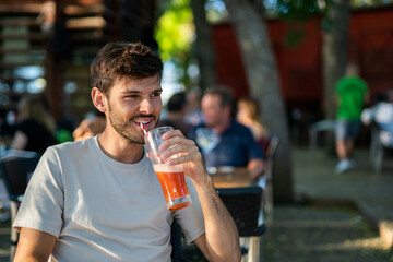 Happy caucasian brunette young man drinking a smoothie with a straw in a terrace