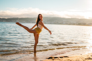 Happy young caucasian woman posing and dancing on the beach at sunset wearing a pareo skirt