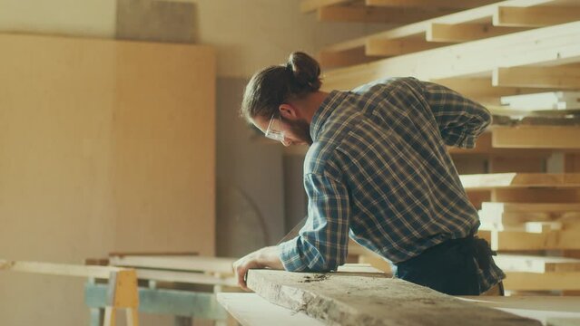 A Man Carpenter in Protective Glasses Sawing Wood Board With Hand Saw.Woodworking. Manual Labor. Factory. Carpentry, Craftsmanship, and Handwork Concept.