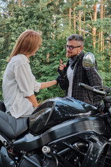 Naklejka premium Middle age couple talking and having fun, sitting on a motorcycle, traveling together on a forest road