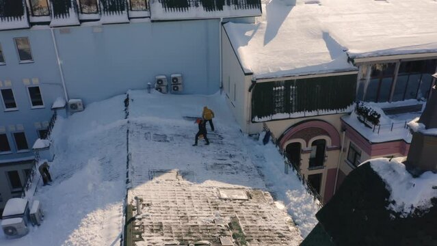 Aerial view squad of janitors cleaning roof after heavy snowfall. Men sweeping snow.