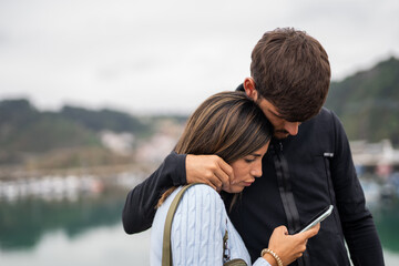 A young caucasian couple cuddling and checking the phone worried