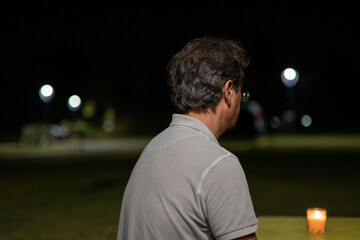 Caucasian man contemplating a candle at night outdoors in a camping