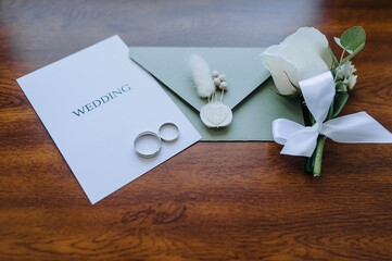 Wedding details and accessories close-up: boutonniere, gold rings, an envelope with a seal with a...