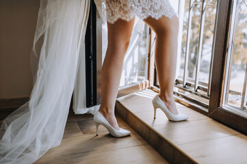 Legs of a beautiful bride in white high-heeled shoes and a long veil near the window. Wedding...