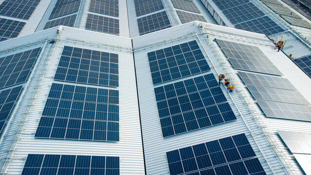 Fly over unidentified Engineering set up a Solar cell on the roof of a large industrial factory. Solar roofs are generating renewable energy for the industry.