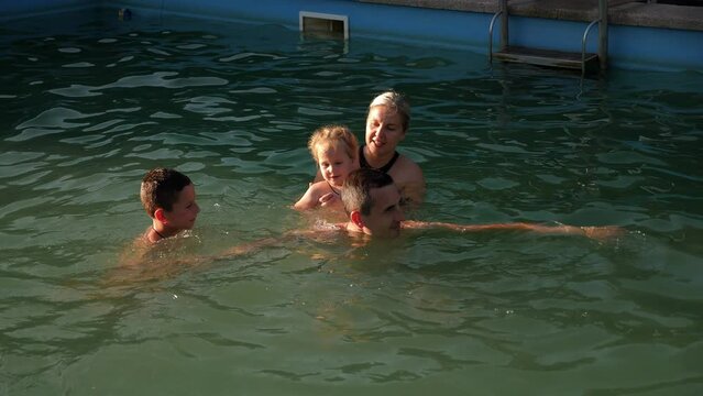 A happy family with children swims in a therapeutic pool with thermal water, they splash water and laugh.