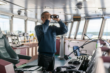 Deck officer with binoculars on navigational bridge. Seaman on board of vessel. Commercial...