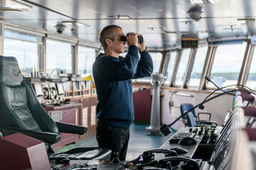 Fototapeta na wymiar Deck officer with binoculars on navigational bridge. Seaman on board of vessel. Commercial shipping. Cargo ship.