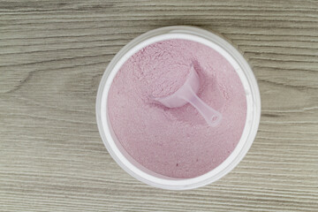 protein powder or bcaa with scoop in plastic jar, on wooden background, top view, flat lay.