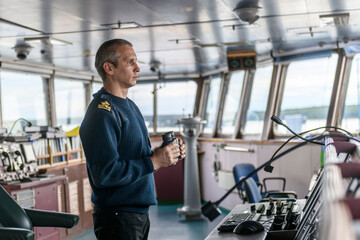 Deck officer with binoculars on navigational bridge. Seaman on board of vessel. Commercial shipping. Cargo ship.