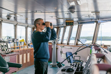 Deck officer with binoculars on navigational bridge. Seaman on board of vessel. Commercial shipping. Cargo ship.