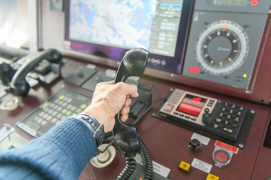 Navigational control panel and VHF radio with hand. Radio communication at sea. Working on the ship's bridge.