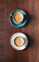 Directly above shot of two cups of coffee on wooden background. Cappuccino or latte with frothy foam, blue coffee cup top view closeup isolated on brown background