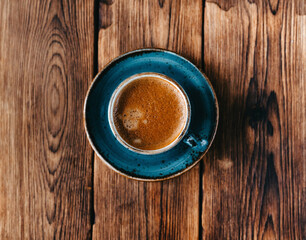 Directly above shot of cup of coffee on wooden background. Cappuccino or latte with frothy foam, blue coffee cup top view closeup isolated on brown background