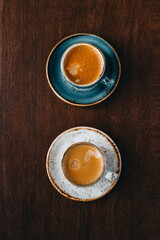 Directly above shot of two cups of coffee on wooden background. Cappuccino or latte with frothy foam, blue coffee cup top view closeup isolated on brown background