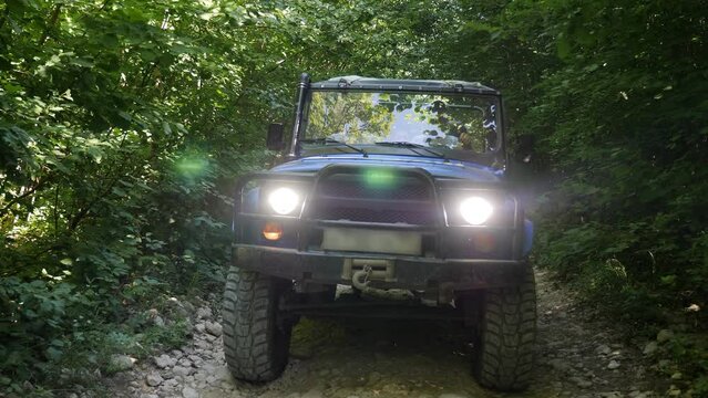 Active extreme recreation in the mountains, young tourists drive along a dirt road with rocks in a jeep high in the mountains among the trees.
