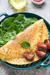Close-up of omelette with fresh spinach leaves and tomato wedges, vertical shot, selective focus