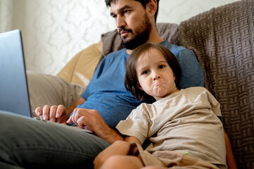 Fototapeta premium The father works at home on a laptop and the child requires attention, wants dad to rub toys with him.