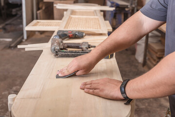 A man uses a piece of sandpaper to smooth out the top of a circular table. Hand sanding a wood surface. A DIY project at a personal workshop.