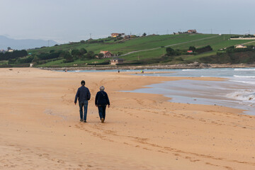 Retired couple strolling on Valdearenas Beach. Liencres, Cantabria
