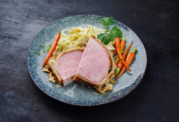 Gebackenes Kasseler Schweinesteak im Teigmantel mit Wirsing Kohl und Baby Karotten serviert als close-up auf einem Design Teller mit Textfreiraum