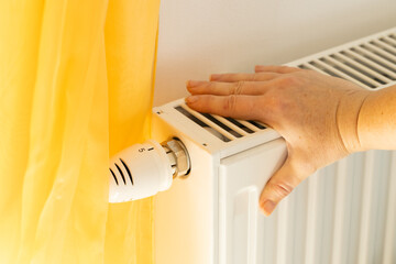 A woman's hand checks if the radiator is heating, Costs of heating the house and apartments, Rising...