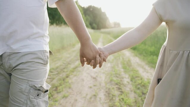 A loving couple walks along the road along the field in the rays of the setting sun. Close-up.