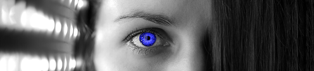 Black and white portrait of a woman with blue eye. The girl's face is illuminated on one side and covered with hair on the other. Over black background. Panoramic banner.