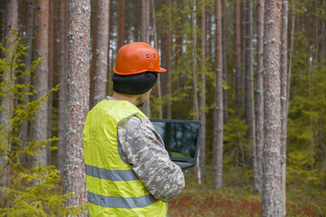 Forest worker worker works in the forest with a computer. Trees are reflected on the computer...