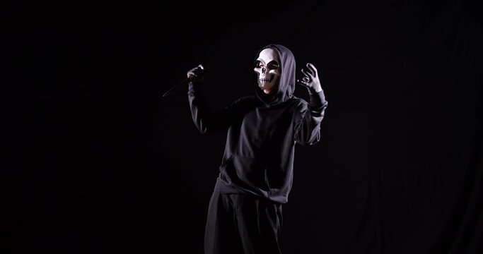 Crazy Man In The Hooded Sweatshirt Wearing Halloween Mask Holding A Knife And Laughing On The Black Background

