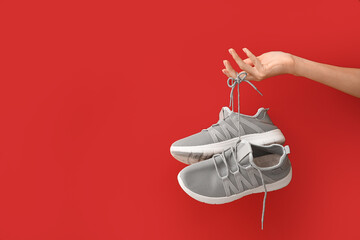 Female hand with grey sneakers on red background