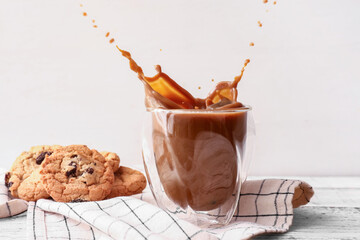 Glass of delicious iced coffee with splashes and cookies on table