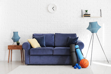 Interior of living room with comfortable sofa and sport equipment near white brick wall